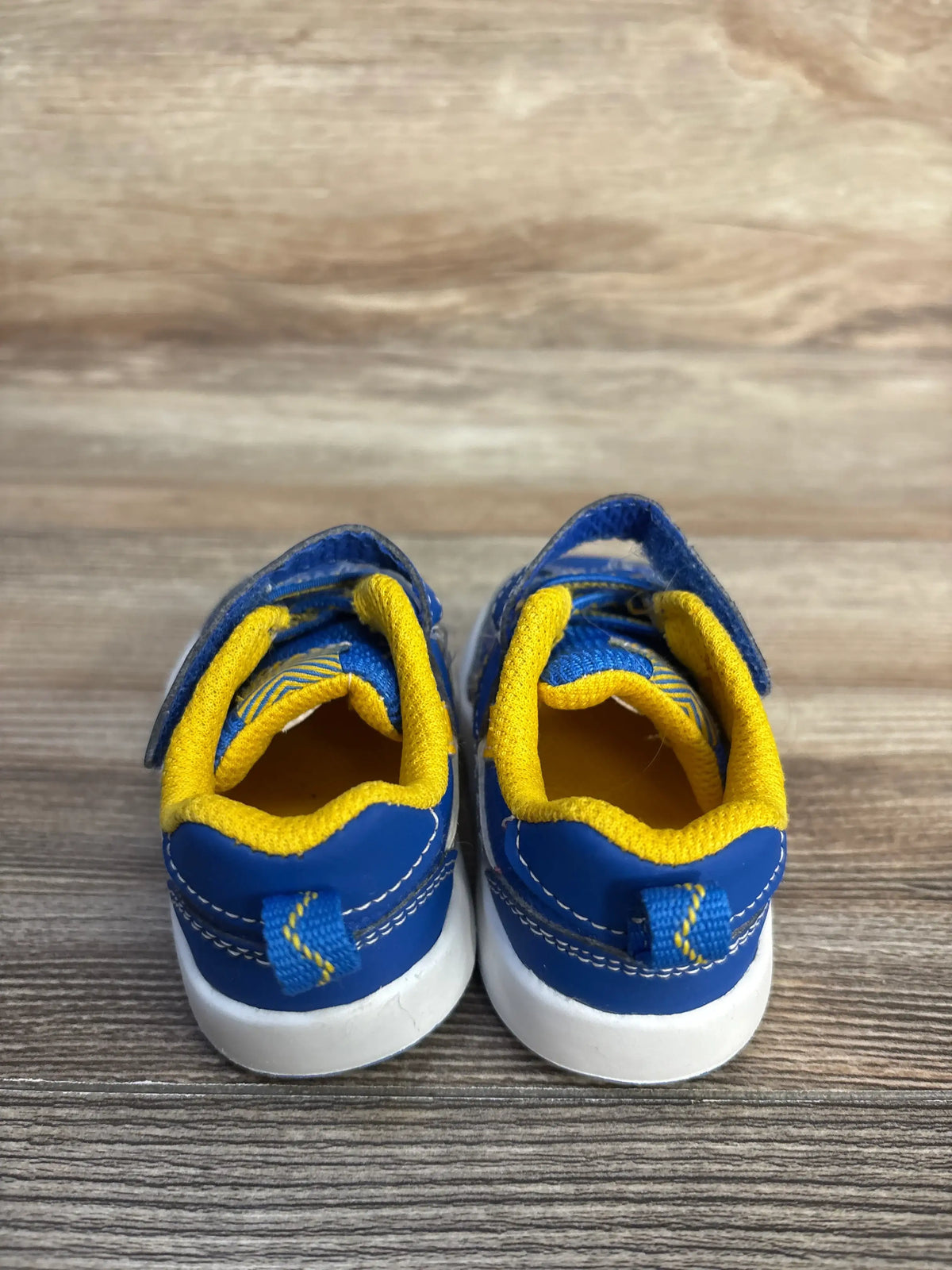 Rear view of Wonder Nation blue sneakers in size 3C showcasing yellow trim and white soles on a wood surface
