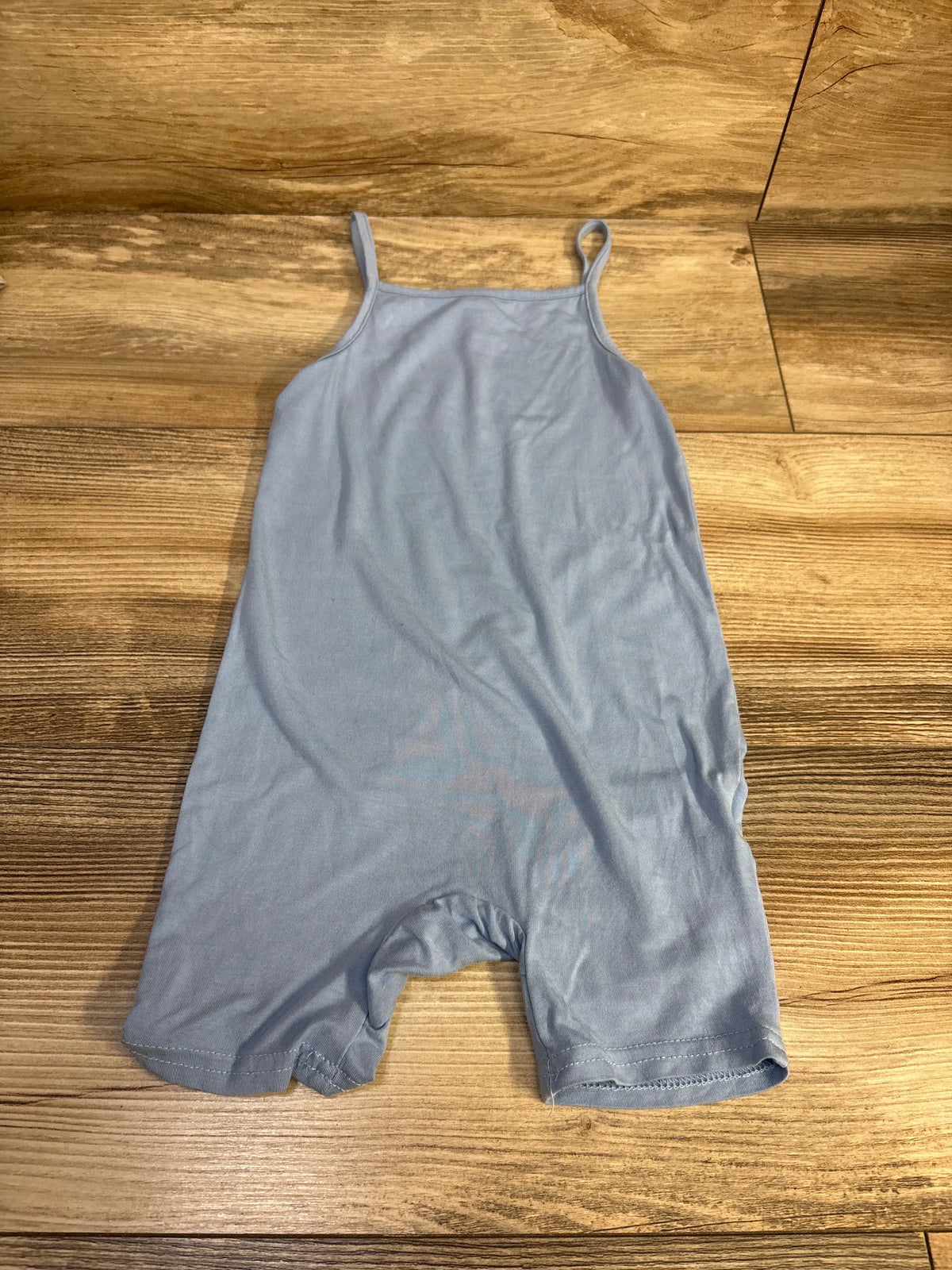 Flat lay of blue toddler tank shortie romper showcasing thin shoulder straps and short legs on a wood floor
