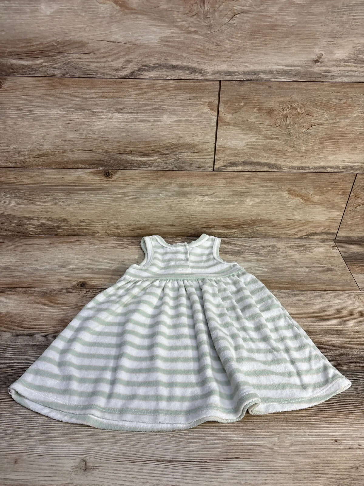 Flat lay of toddler terry cloth dress showing sleeveless bodice and gathered skirt with pale green and white stripes on wood floor