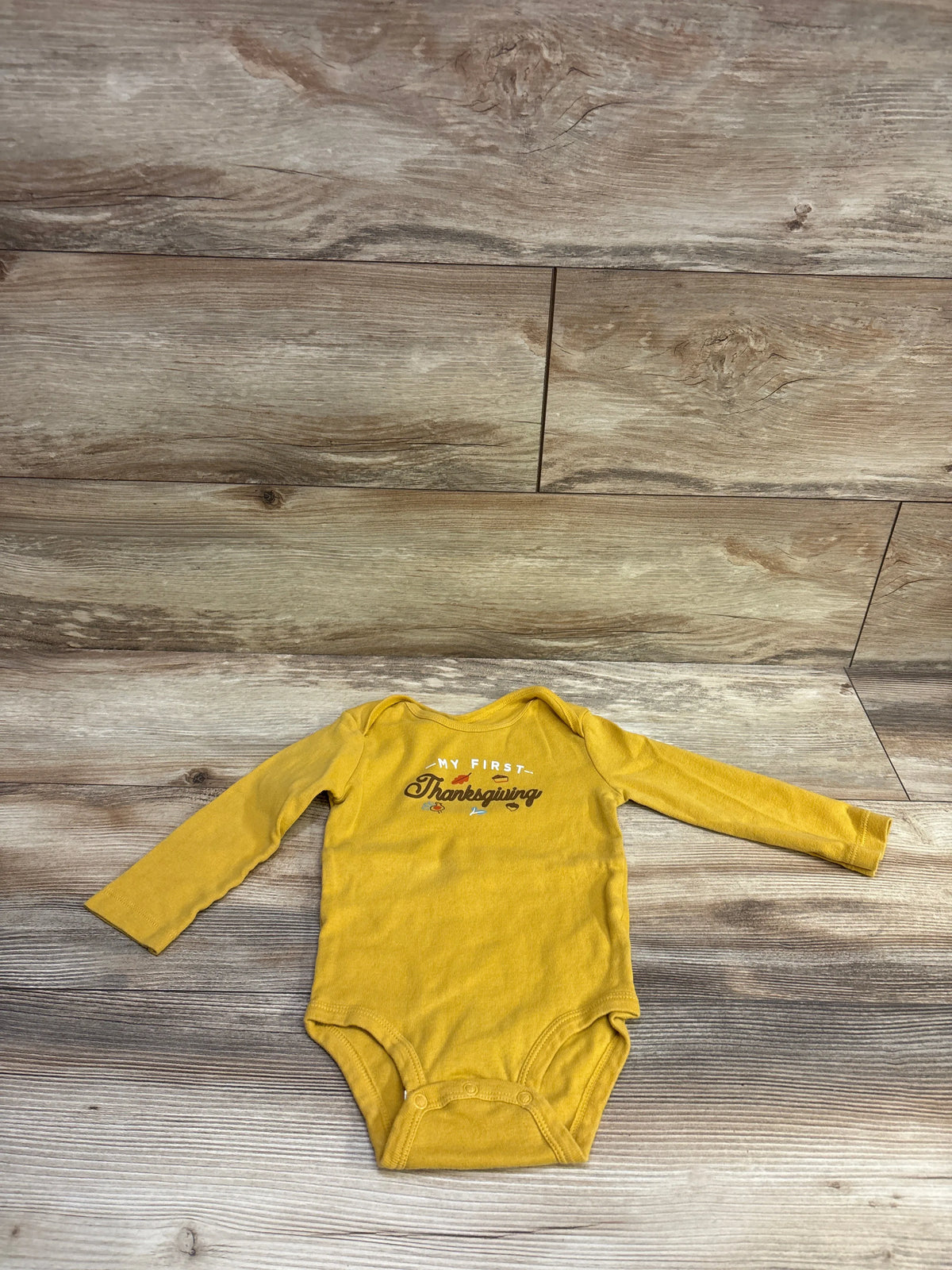 Front view of Carter’s My First Thanksgiving bodysuit showcasing yellow long sleeves and snap closures on a wood background