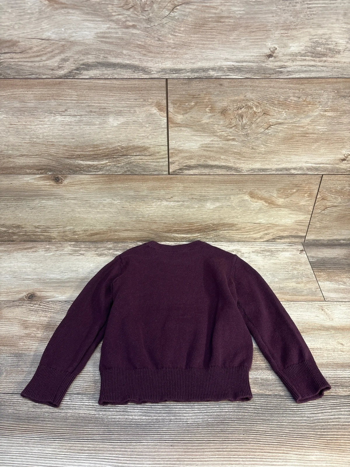 Back of Baby Gap Triceratops sweater, eggplant 2T, knit texture and ribbed hem on wood floor