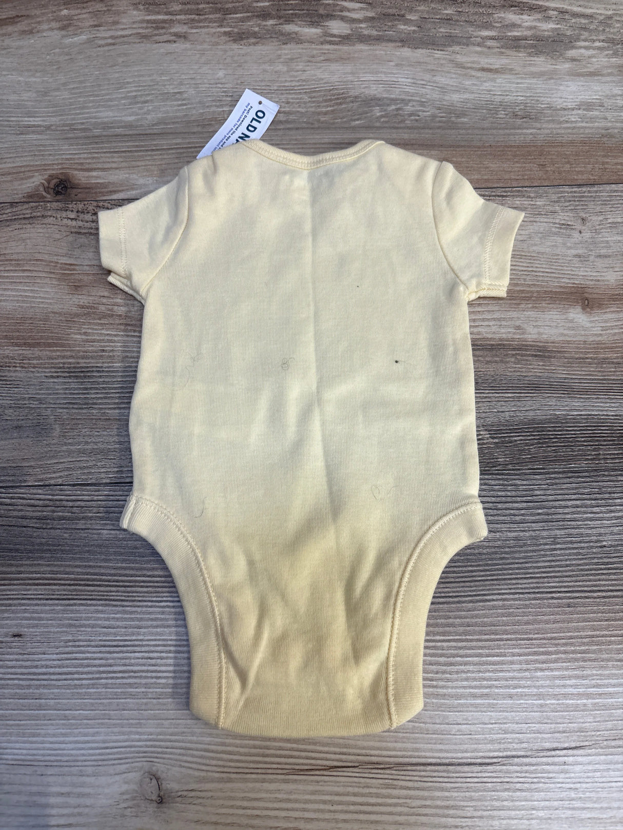 Light yellow short sleeve baby bodysuit on wooden background, resale kids clothing