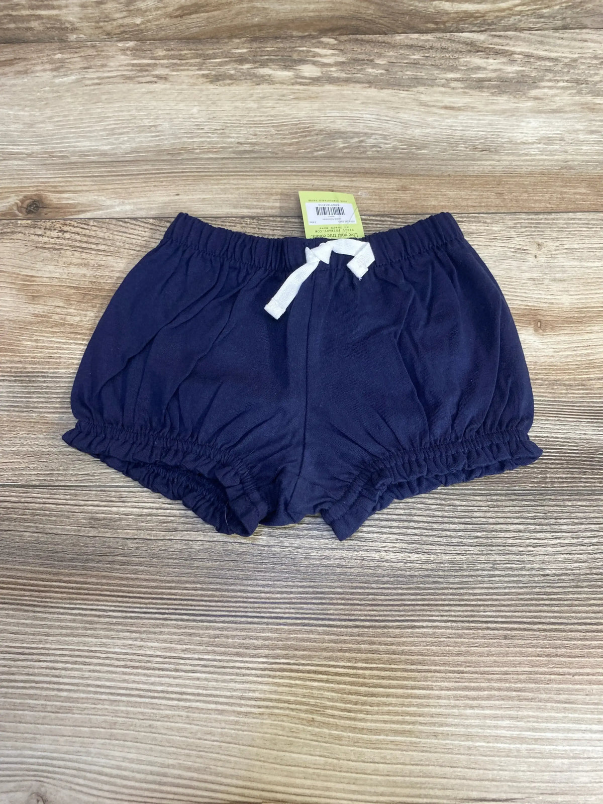 Top-down view of navy baby bloomer shorts 3 to 6 months showing elasticized waist, white drawstring and ruffled leg openings on wood background