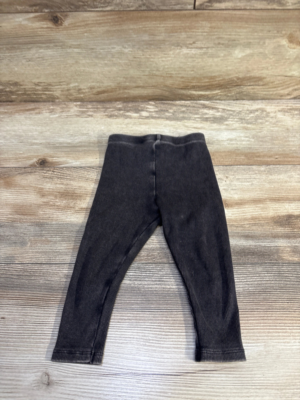 Top-down view of grey ribbed baby leggings size 12M showcasing elastic waistband and ribbed texture on light wood background