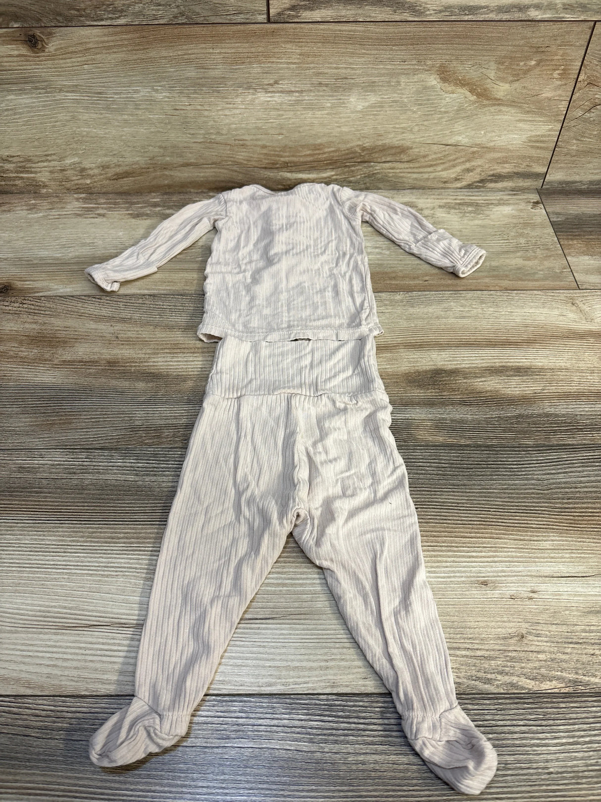 Light beige ribbed baby two-piece outfit with long sleeves and footed pants on wood floor
