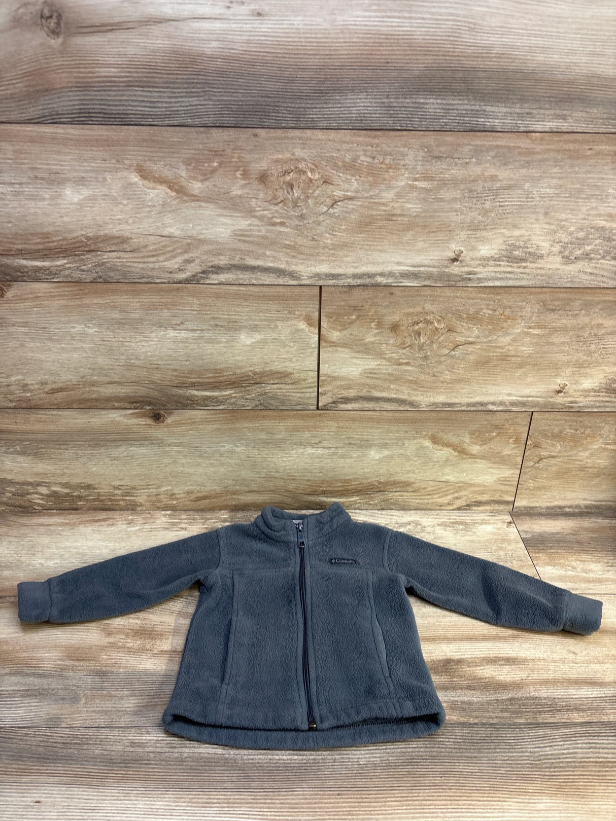 Flat-lay of Columbia toddler grey fleece full-zip jacket showcasing front zip, side pockets, and mock collar on wood background