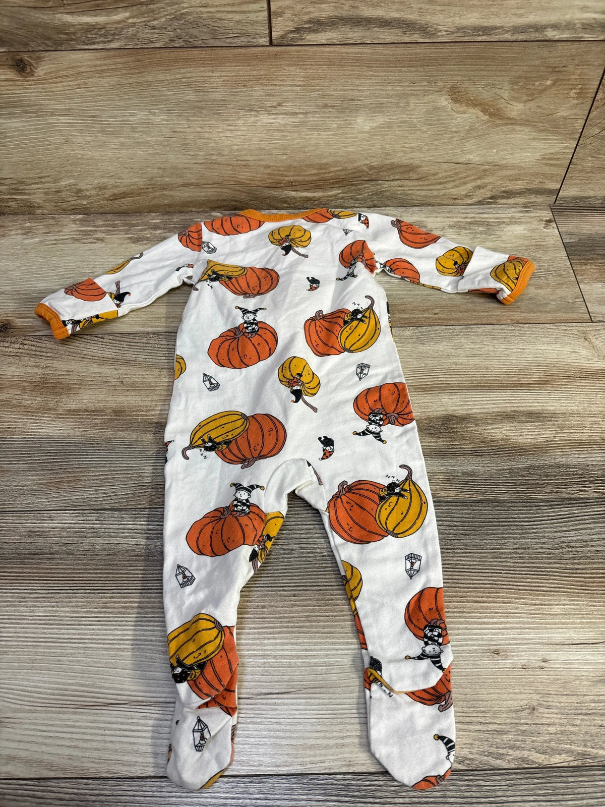 Front view of YKK Halloween pumpkin sleeper showcasing white fabric with orange and yellow pumpkin print, laid flat on wood flooring
