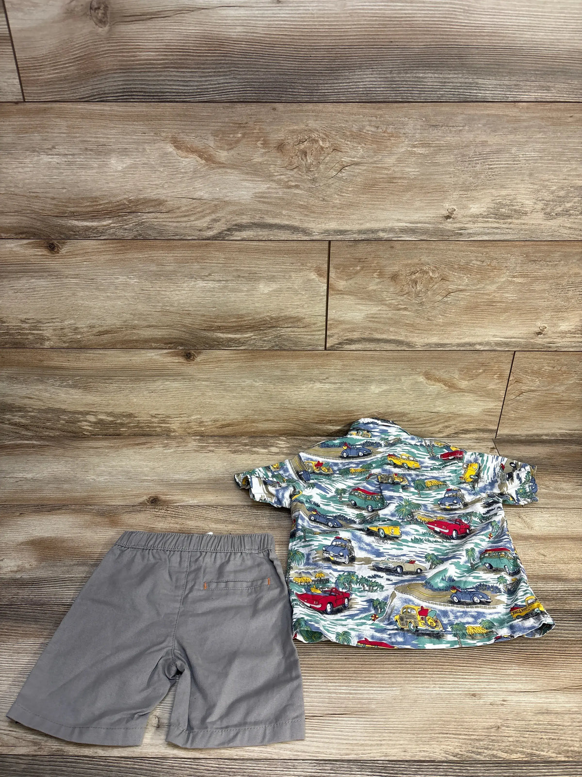 Top-down view of Bugle Boy toddler shirt and shorts set showcasing a colorful car-print shirt and gray shorts on a wood floor