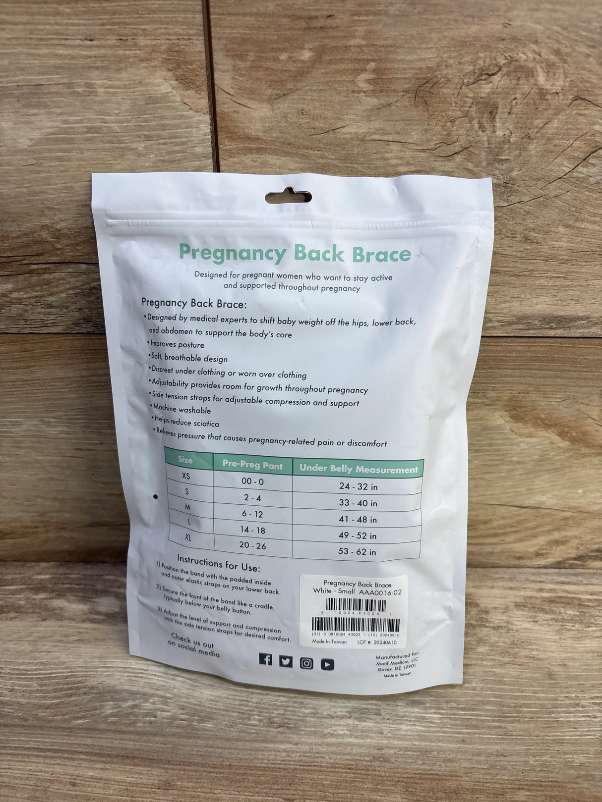 Rear view of Motif Pregnancy Back Brace package showing Pregnancy Back Brace headline, size chart and usage instructions on a wooden floor background