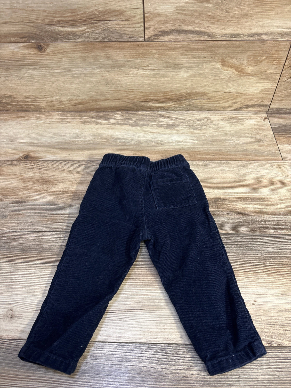 Back view of toddler navy corduroy pants showing elastic waistband and back patch pocket on wood floor background
