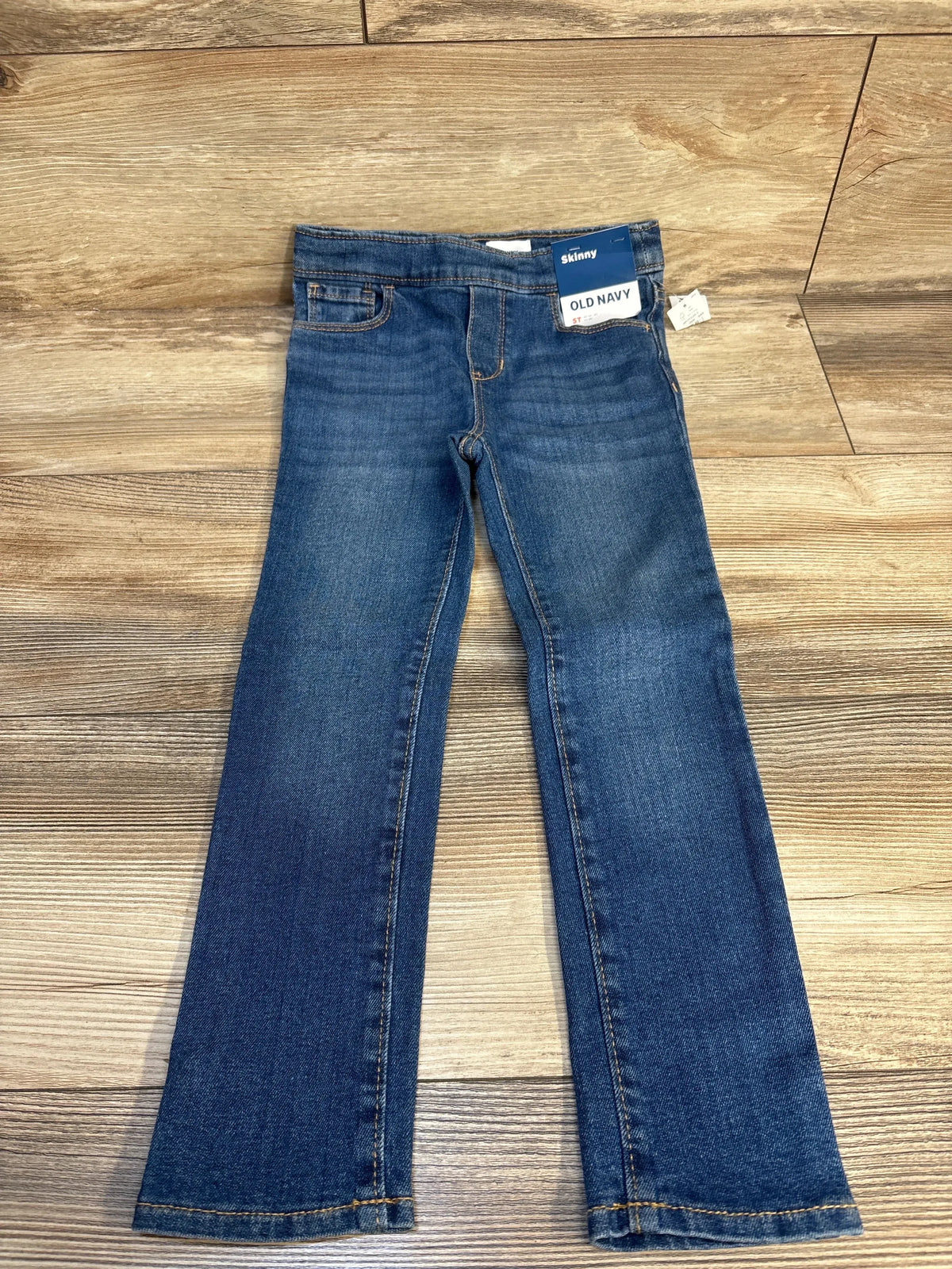 Front view of new Old Navy blue skinny jeggings, size 5T, laid flat on a wood floor