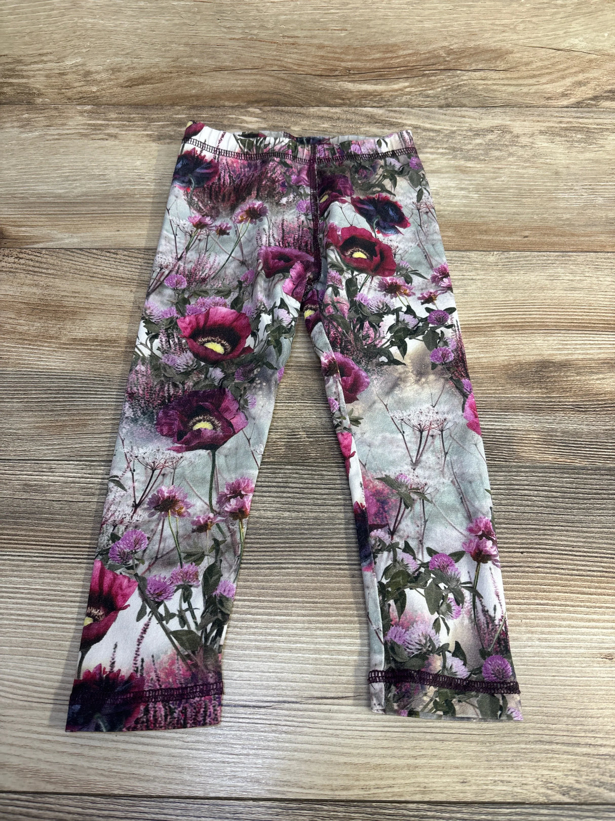 Flat lay of Molo Floral Stefanie leggings size 2T showcasing all-over pink and purple floral print and elastic waistband on wood background