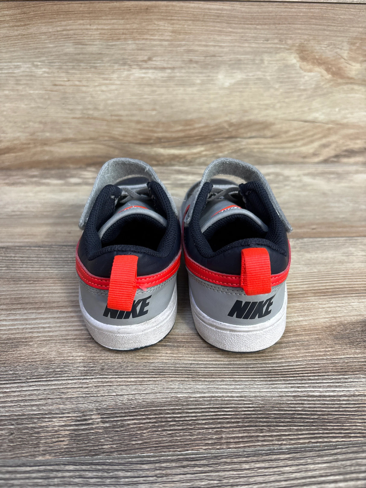 Back view of toddler Nike sneakers with gray, black, and red accents on wooden floor