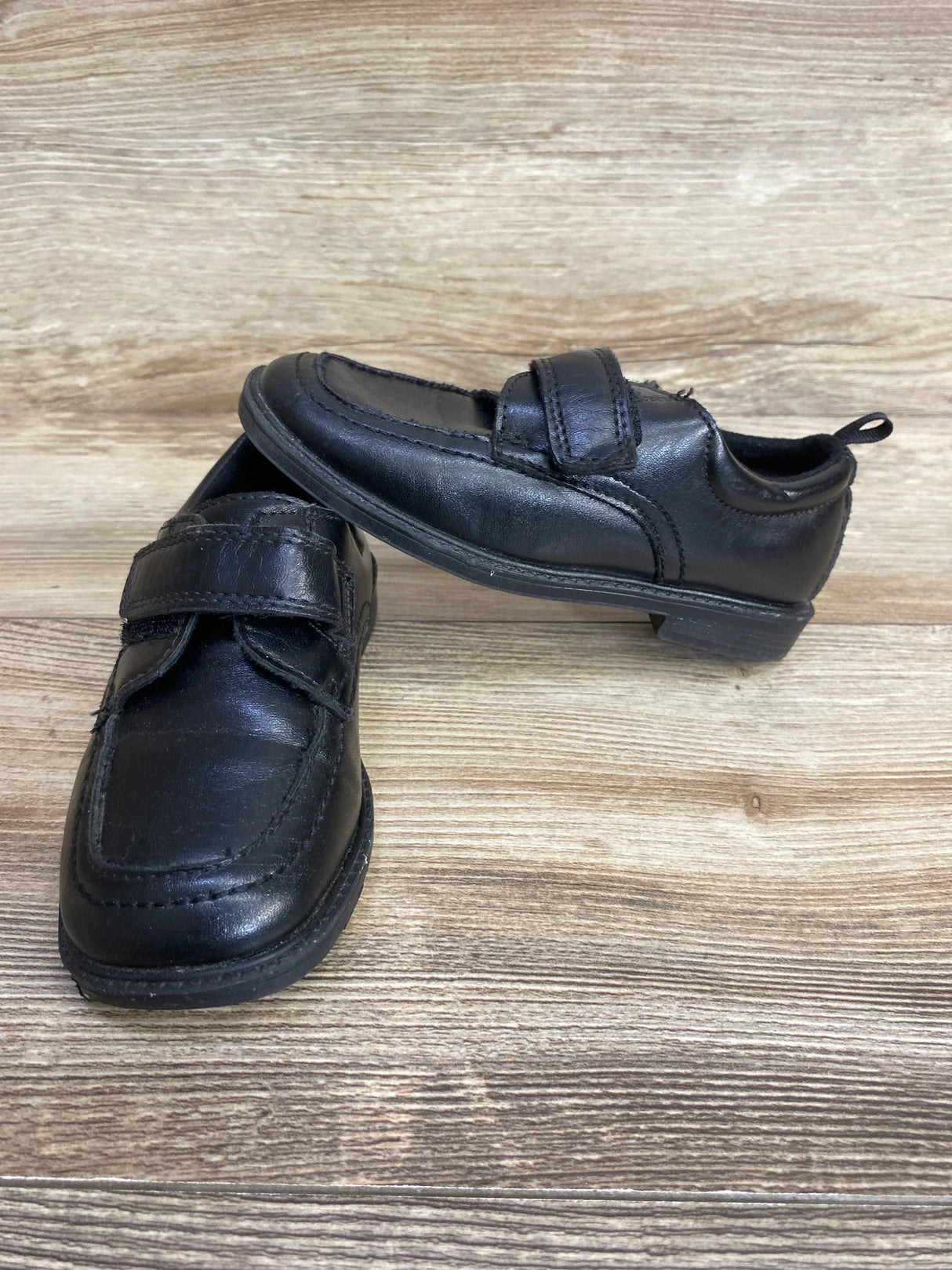 Black boys' dress shoes with velcro strap on wooden surface