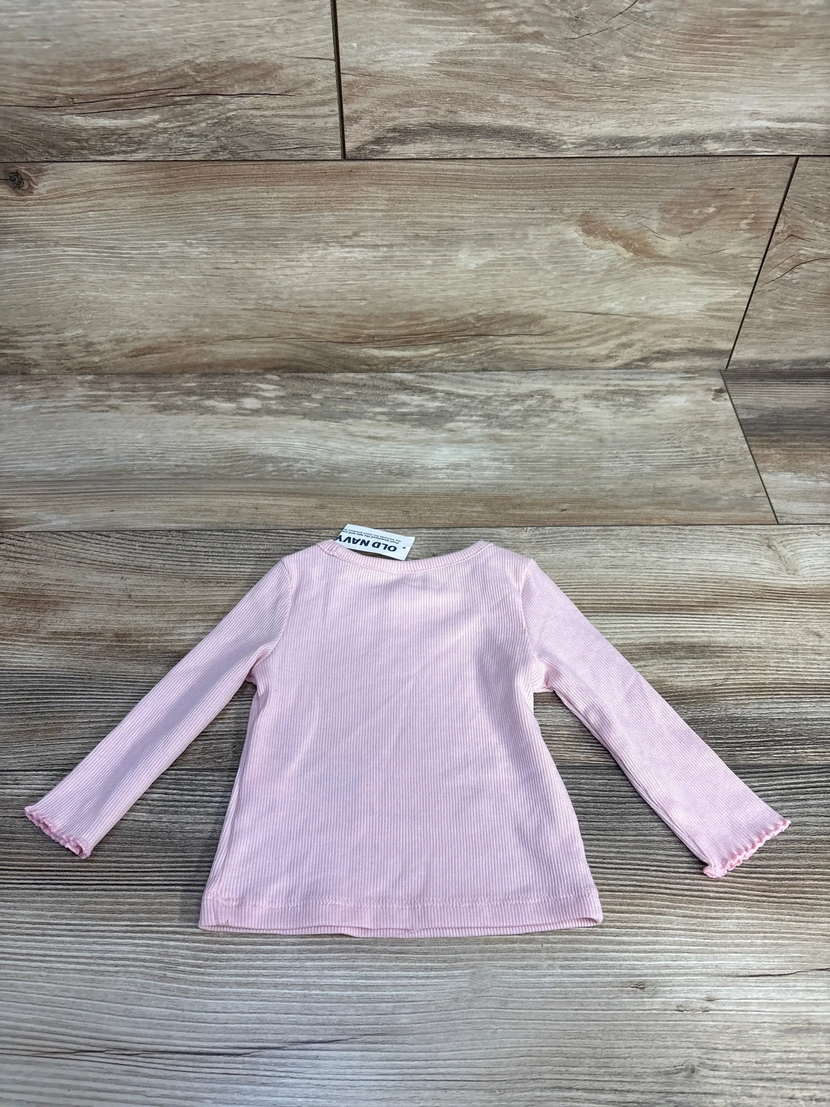 Back view of a pastel pink ribbed long sleeve toddler shirt on wood floor background