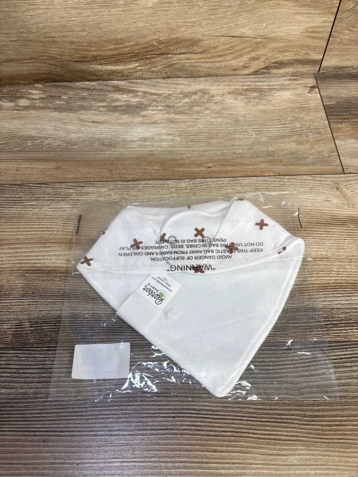 Top view of NEW Parker baby bandana bib showcasing white fabric with brown plus signs in clear packaging