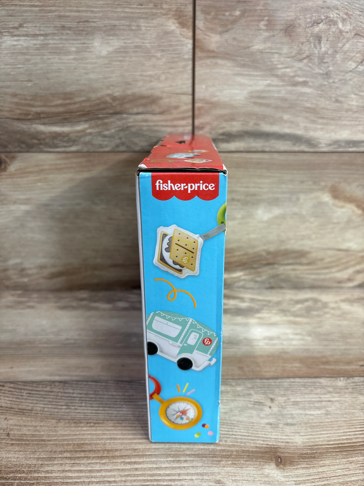 Side panel of Fisher-Price S'more Fun Camping Gift Set box showing s'more illustration, camper toy, and compass on wood surface