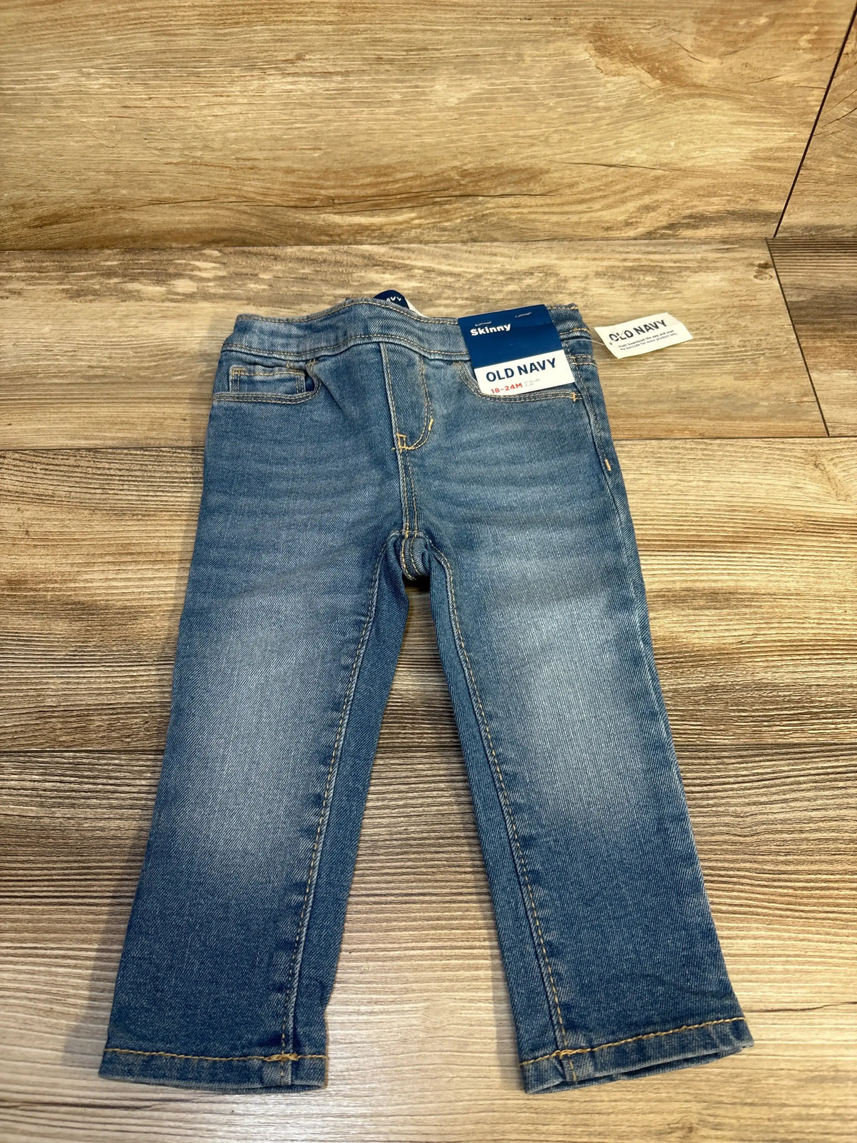 Flat lay of NWT Old Navy skinny jeggings in light blue wash denim with pull on waistband and hangtags on wood plank floor
