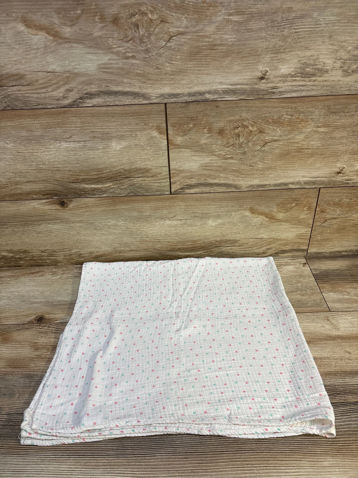 Soft baby muslin blanket with pink and mint polka dots on wood floor, ideal for newborns and toddlers
