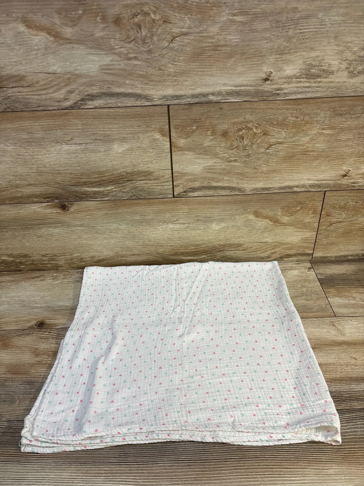 Soft baby muslin blanket with pink and mint polka dots on wood floor, ideal for newborns and toddlers