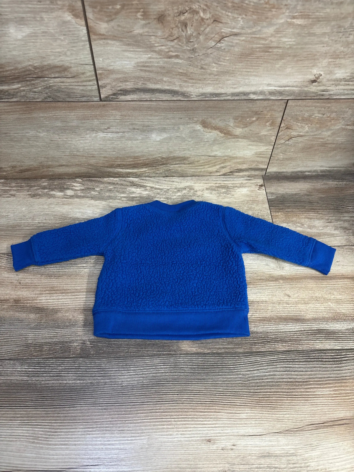 Blue textured toddler sweater with ribbed cuffs on wooden floor