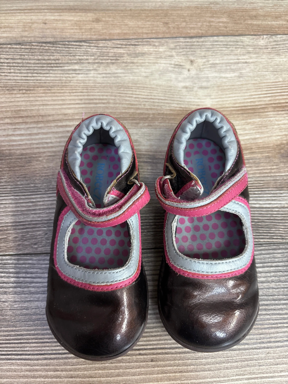 Top view of Robeez faux leather Mary Jane sneakers (size 7C) showcasing pink trim, Velcro strap, and polka-dot insoles on wooden floor
