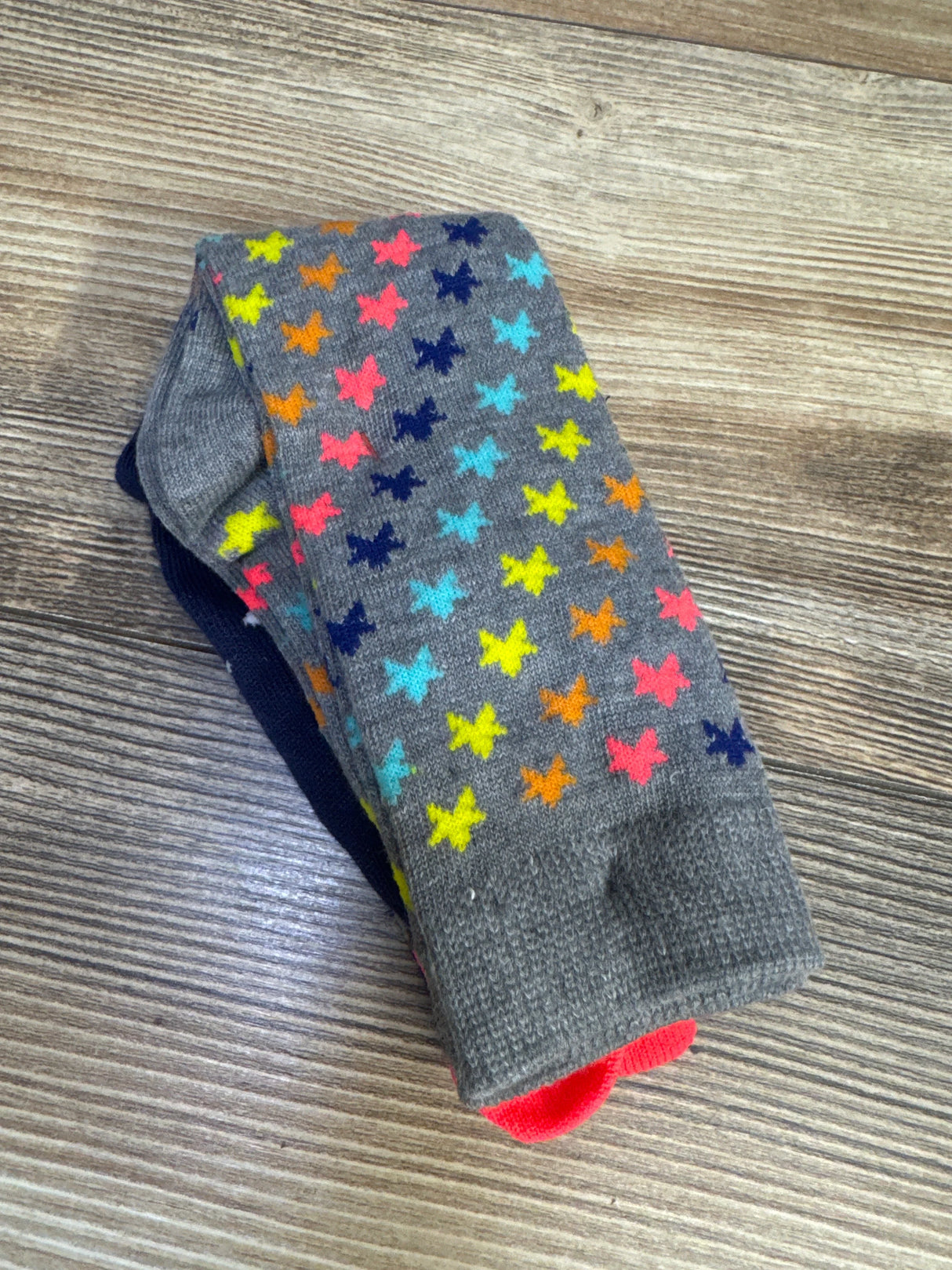 Top down view of knee high socks 2-pack showcasing a gray pair with multicolored star pattern and a solid navy pair on a wood surface