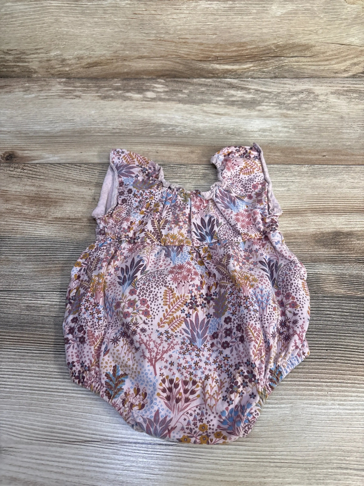 Flat lay of pink floral bubble romper (size 3-6 months) showing ruffled shoulder straps and elastic leg openings on wood background
