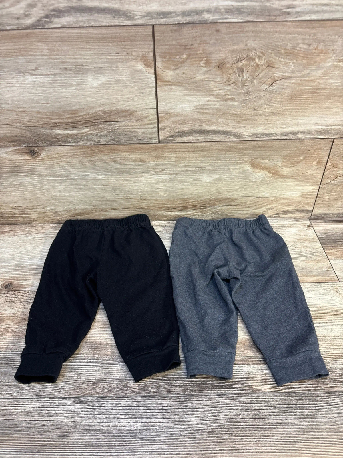 Top view of Cat and Jack two pack pull on pants in black and gray showcasing elastic waists and cuffed hems on a wood look floor