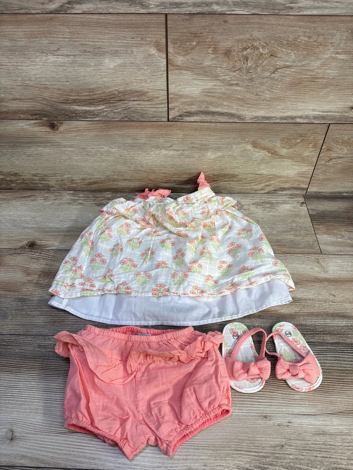 Flat lay of Haute Hippie floral dress set with white dress, pink bloomers, and bow sandals on a wood surface