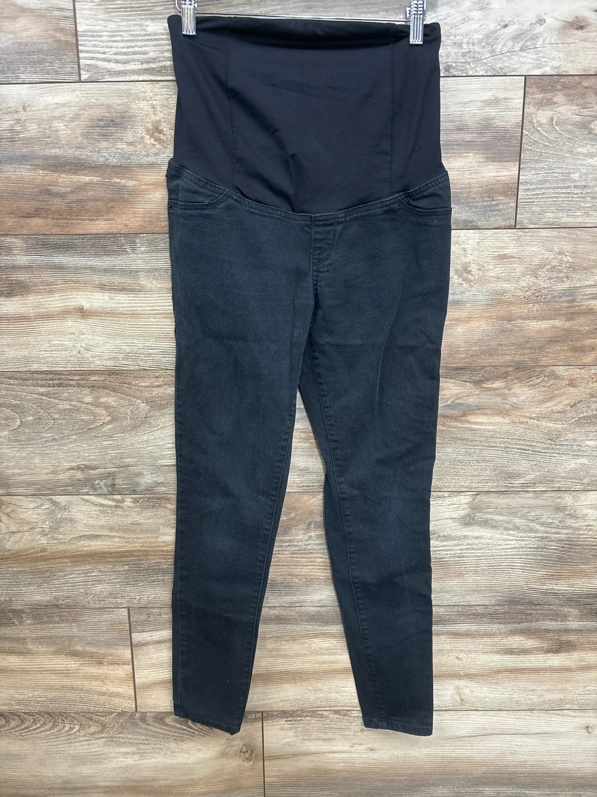 Front view of maternity crossover-panel skinny jeans in black showing crossover belly panel and skinny legs on wood floor