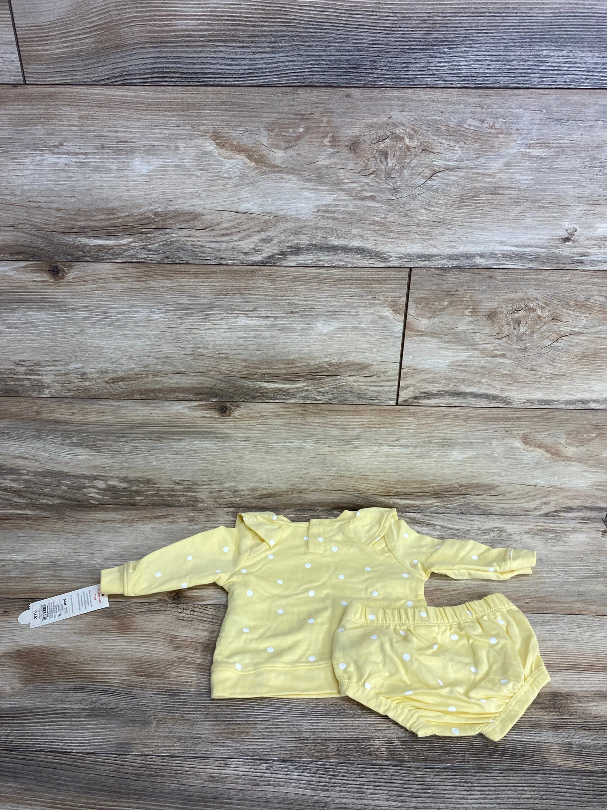 Yellow polka dot long sleeve baby top and matching bloomer shorts on wood background
