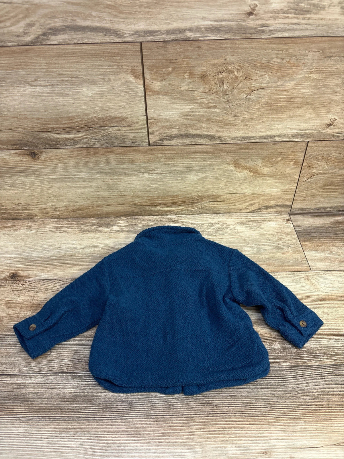 Back view of Old Navy toddler utility shacket showing textured blue fleece and buttoned cuffs on wood plank background