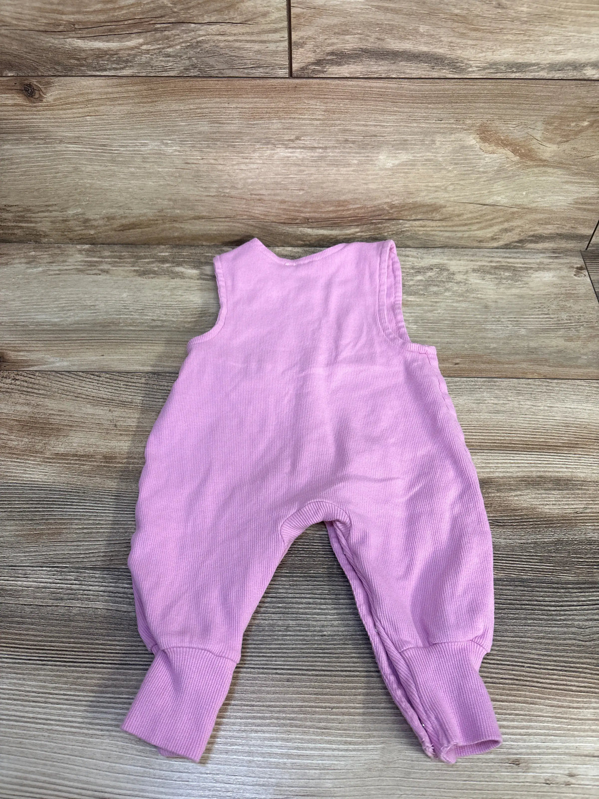 Front view of Burt’s Bees Baby sleeveless pink ribbed jumpsuit showcasing cuffed legs on a wood-grain background