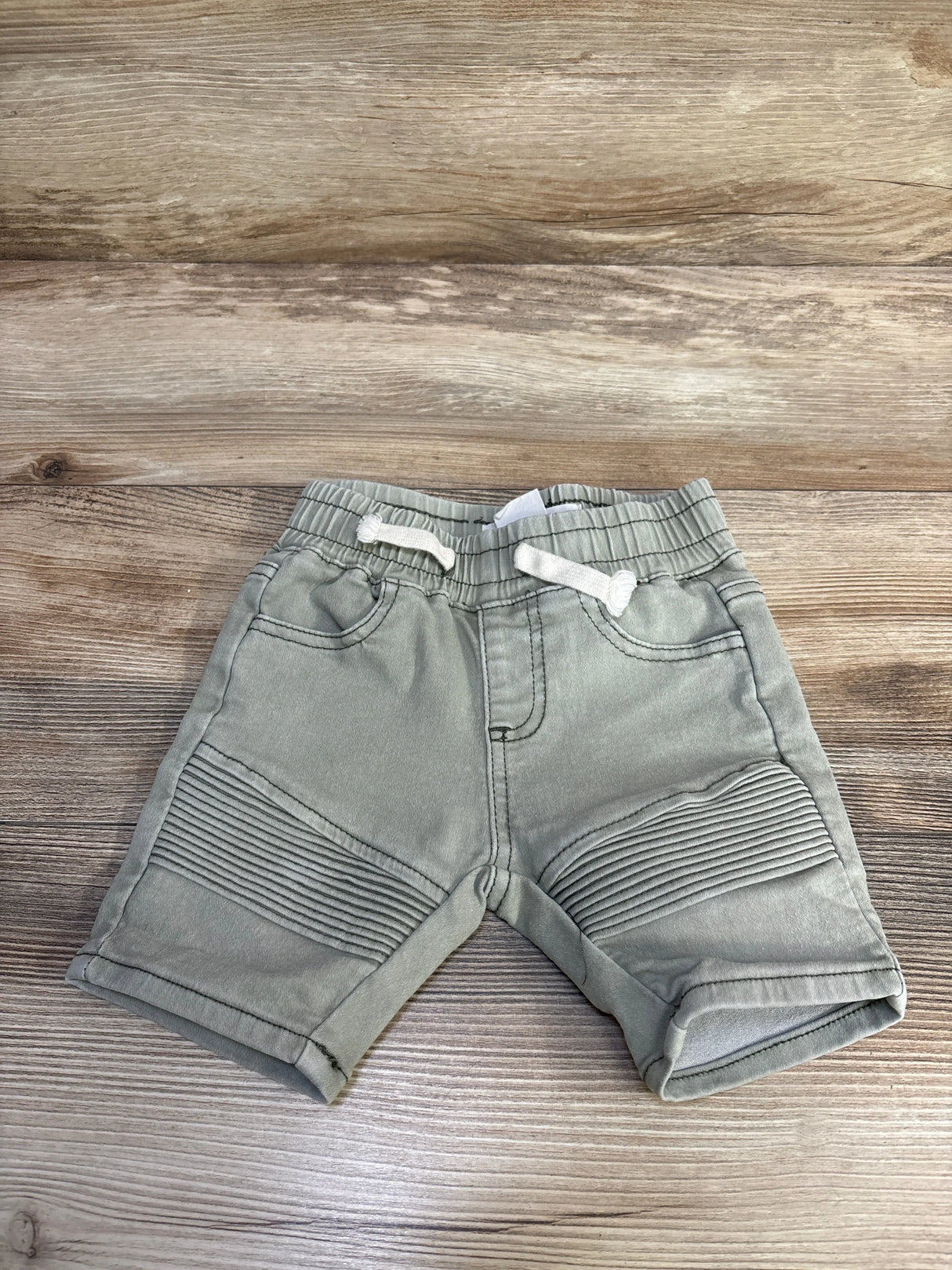 Front view of green Cotton On Baby moto shorts 6-12m showing ribbed knee panels and drawstring waist on wood background