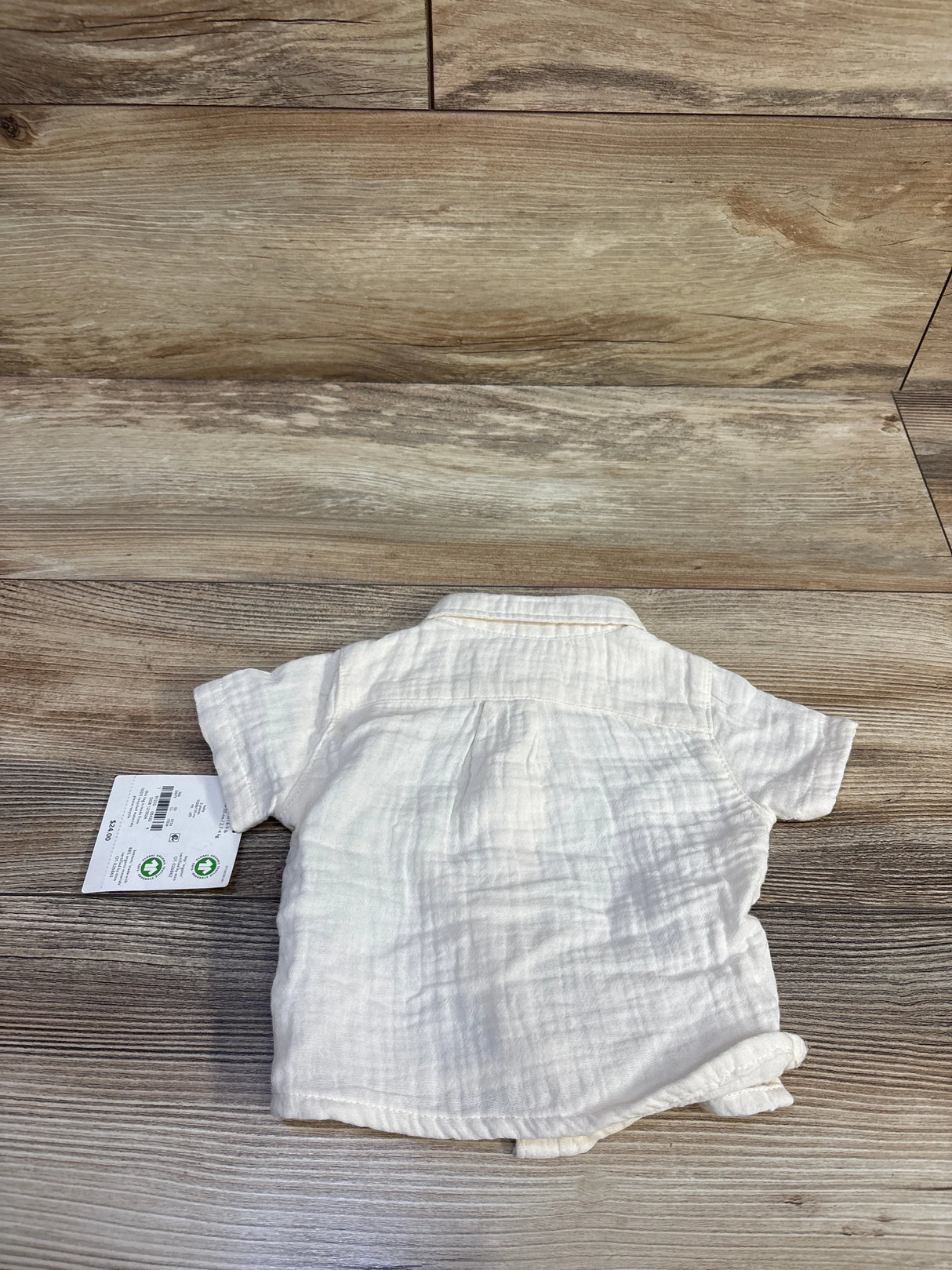 Back view of newborn Little Planet organic button-up shirt in ivory showcasing short sleeves and textured muslin fabric on wood floor background