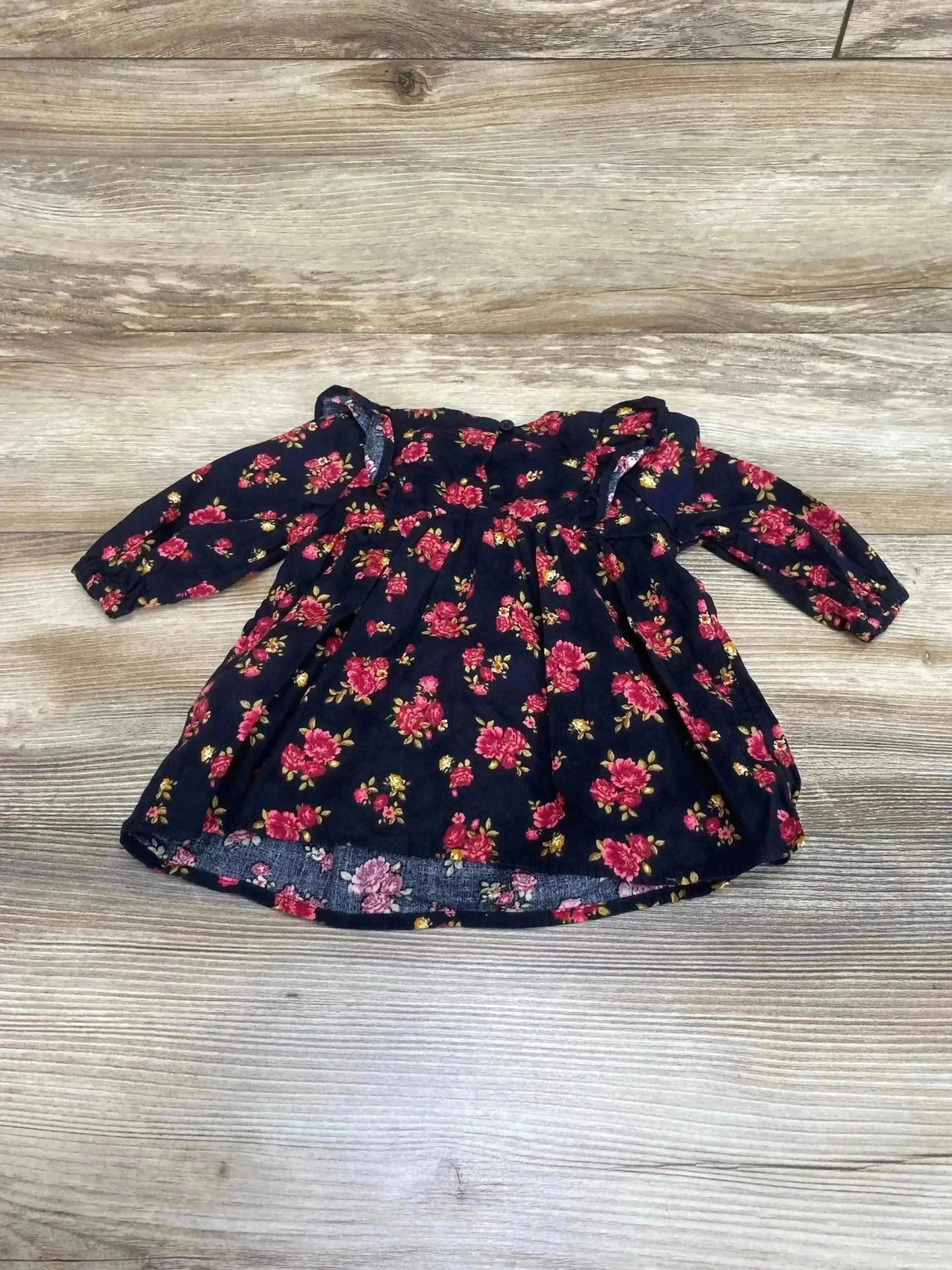Flat lay of Old Navy floral ruffle baby dress 0-3M showing long sleeves, ruffled yoke and pink rose print on navy wood floor