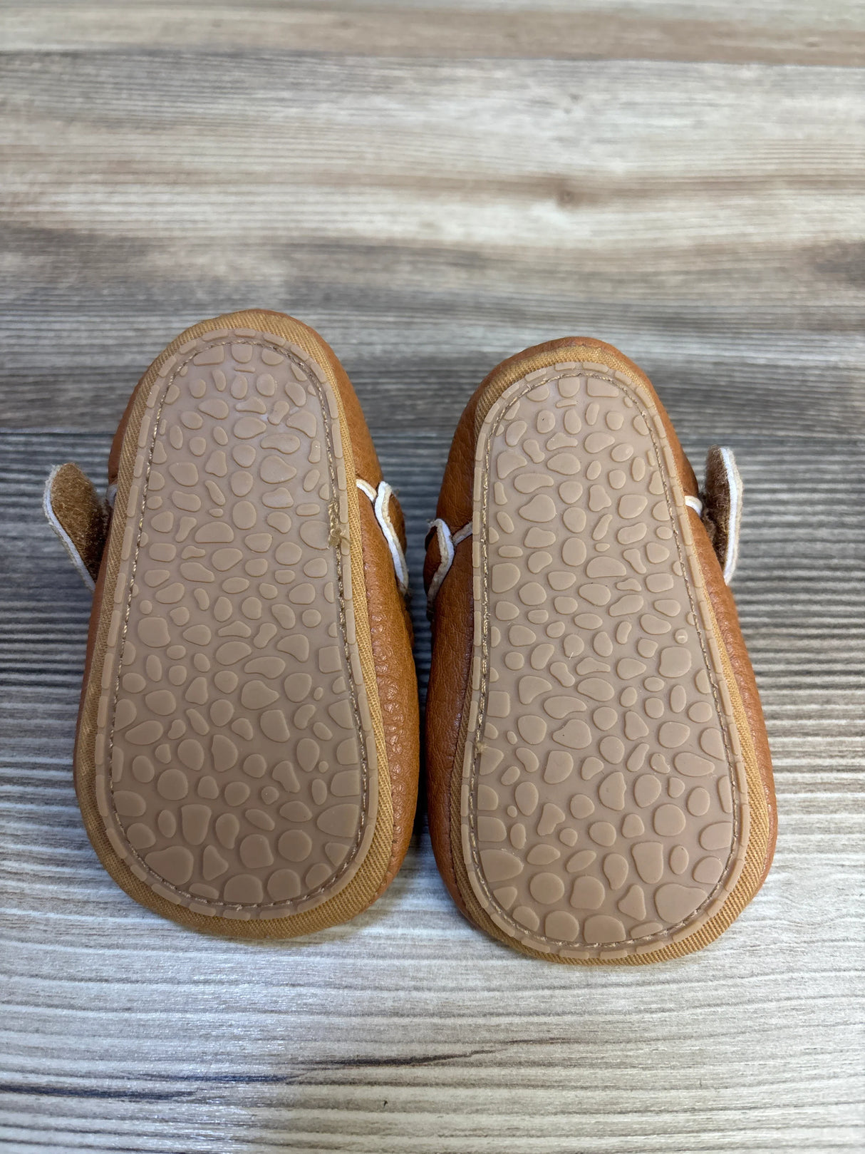 Brown baby shoes with textured rubber soles on a wooden surface