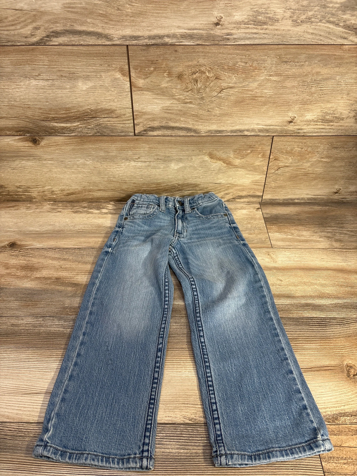 Front view of Cody James boys' light wash relaxed boot jeans size 5T showing faded knees and bootcut legs on wood floor