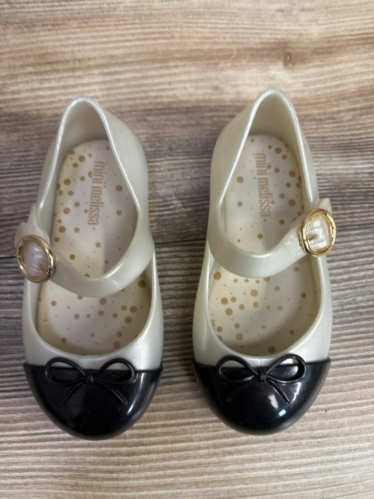 Pair of toddler girls black and white mini melissa Mary Jane shoes with bow detail on wooden surface