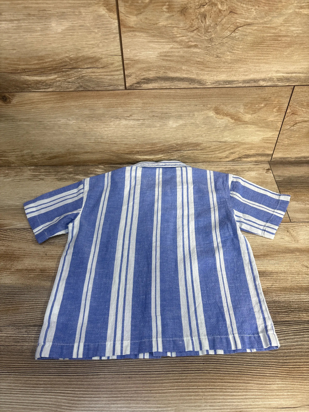 Back view of H&M striped button-up resort shirt, size 2T, showcasing blue and white vertical stripes on wood floor