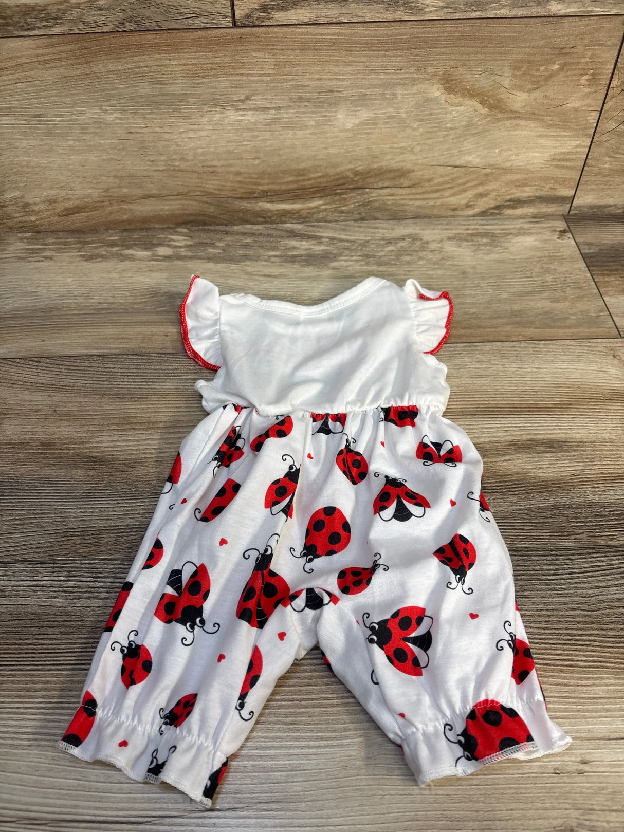 White baby romper with red ladybug print and ruffle sleeves on wood floor