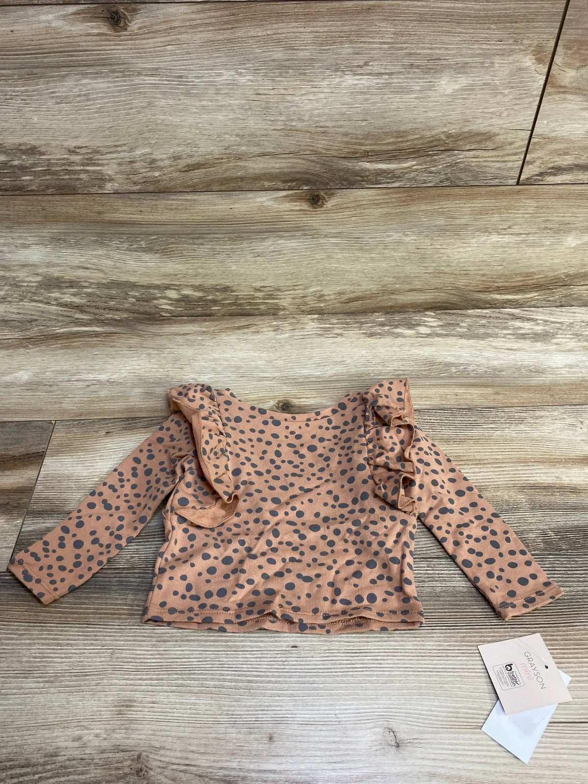 Baby long sleeve polka dot ruffle shirt on wooden background, clothing tag visible