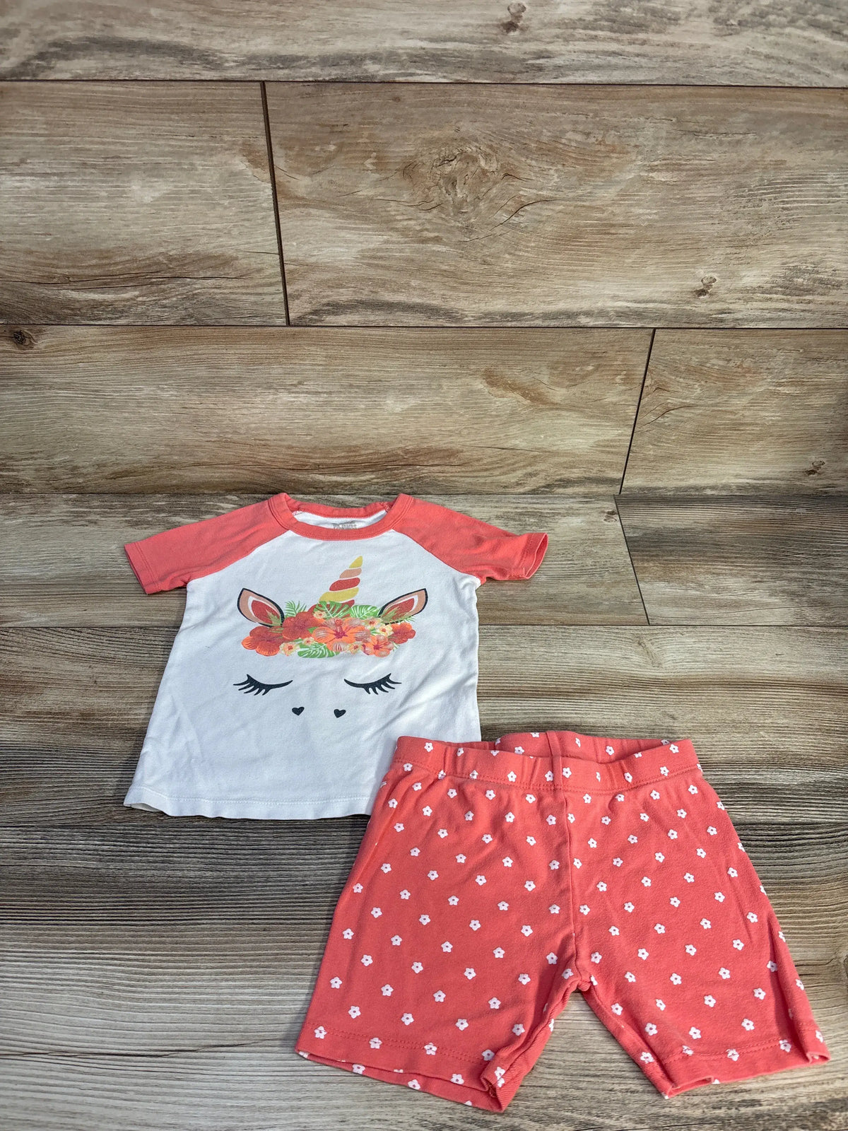 Top view of Member’s Mark 4T two-piece pajama set showing a unicorn top and coral floral-print shorts on wood-look flooring