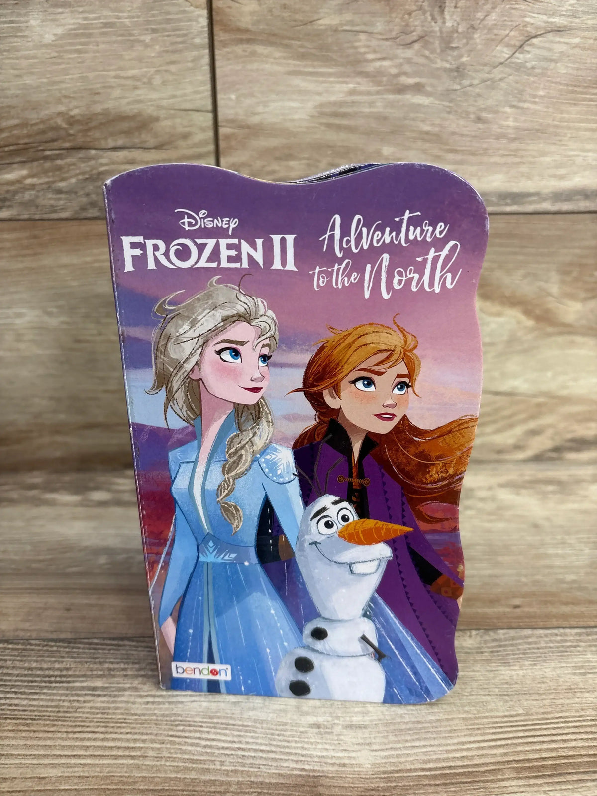 Front view of Disney Frozen II Adventure to the North board book showing cover illustration of Elsa, Anna, and Olaf on a wooden surface