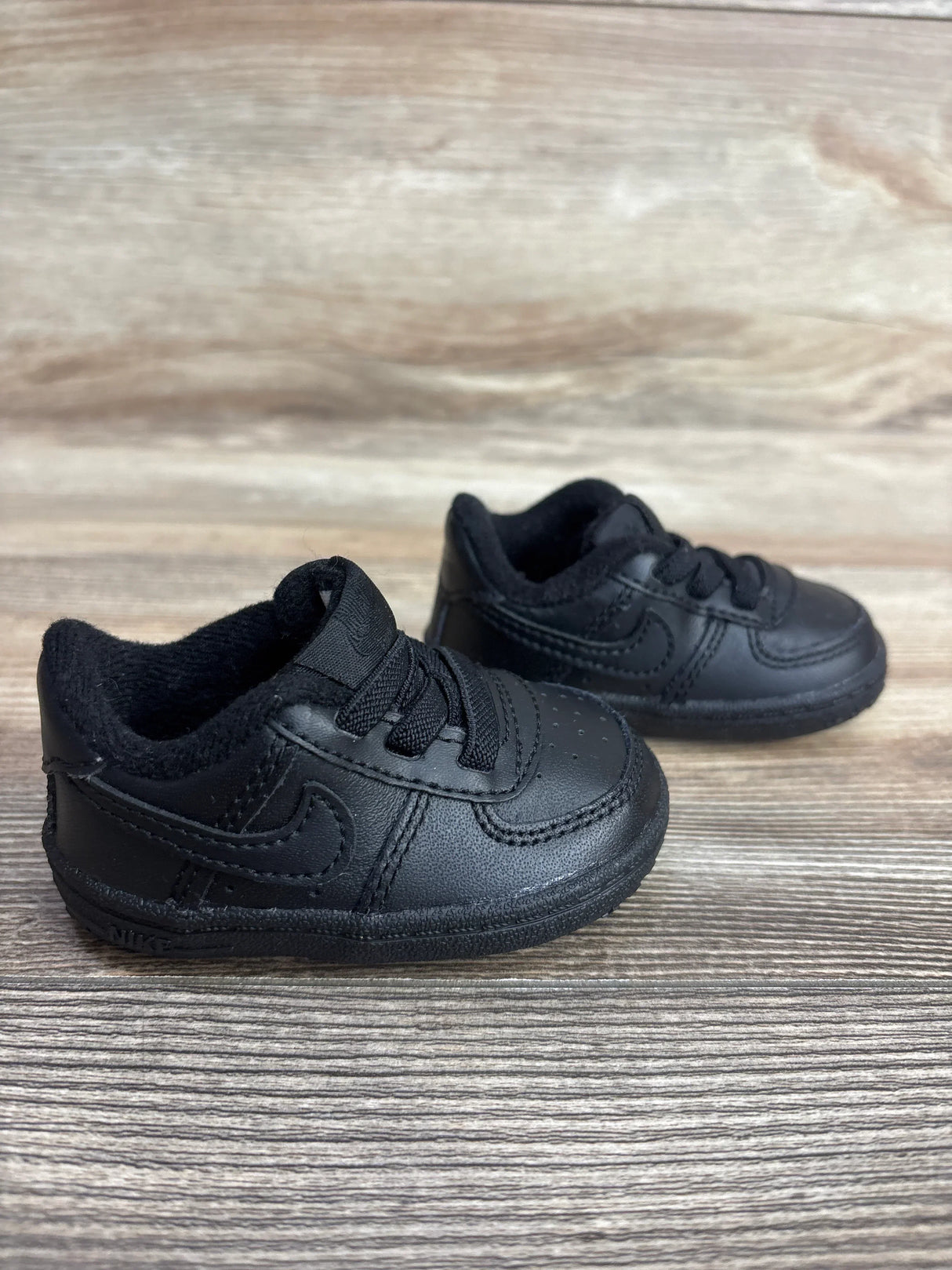 Pair of black toddler Nike sneakers on a wooden surface, showcasing baby shoes for resale
