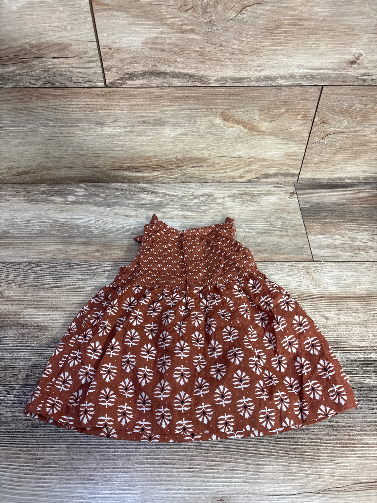 Brown Just One You sleeveless baby dress with white leaf print on a wood background