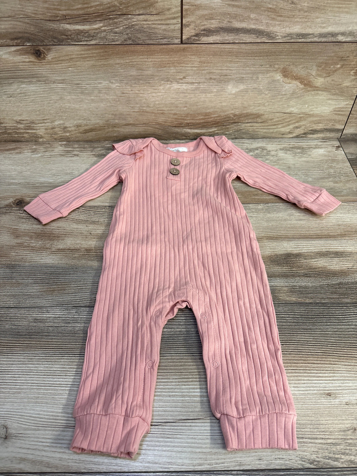 Pink ribbed long-sleeve baby onesie with wooden buttons on wooden floor