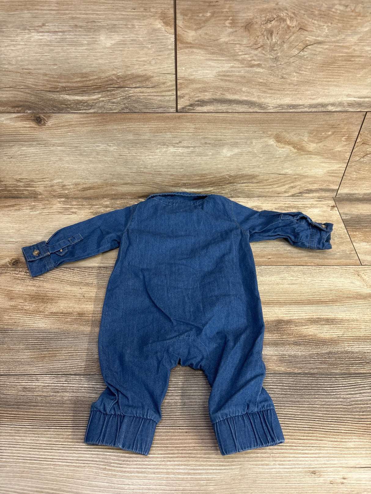 Back view of Cat & Jack chambray newborn jumpsuit showing long buttoned sleeves and cuffed legs on wooden floor