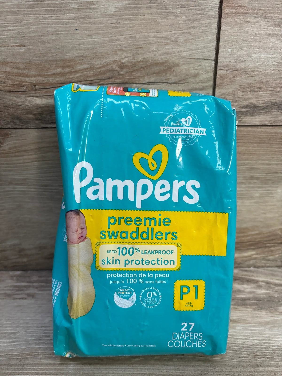 Front view of Pampers Preemie Swaddlers 27-count pack, teal packaging saying 'leakproof skin protection', on wood background